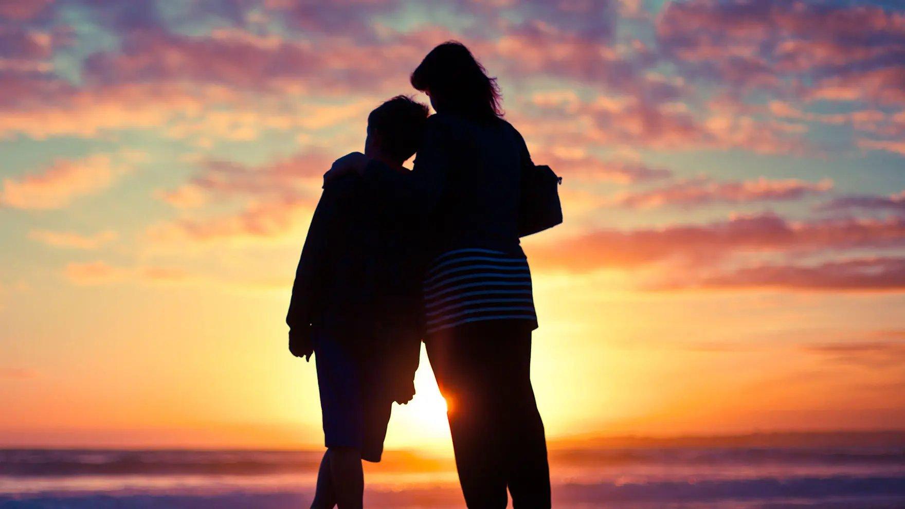 Dos personas abrazándose en la playa con la puesta del sol de fondo