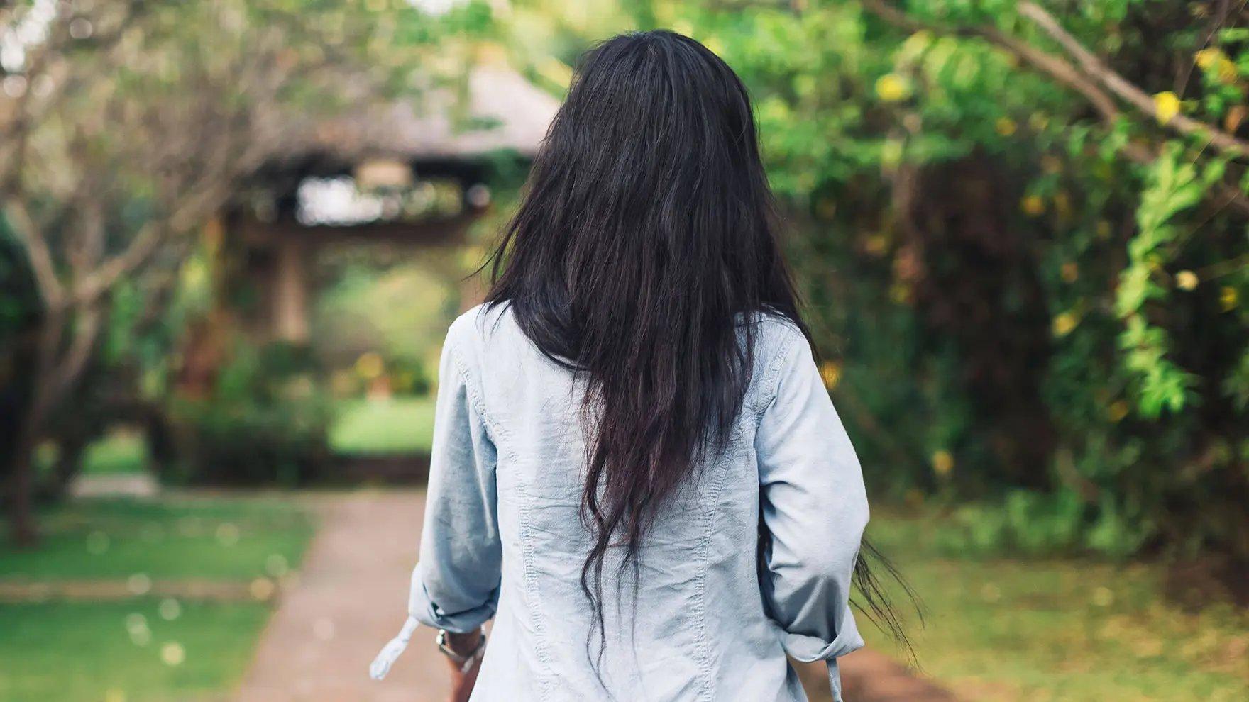 Mujer con cabello largo y oscuro, y una camisa azul, de espaldas a la cámara